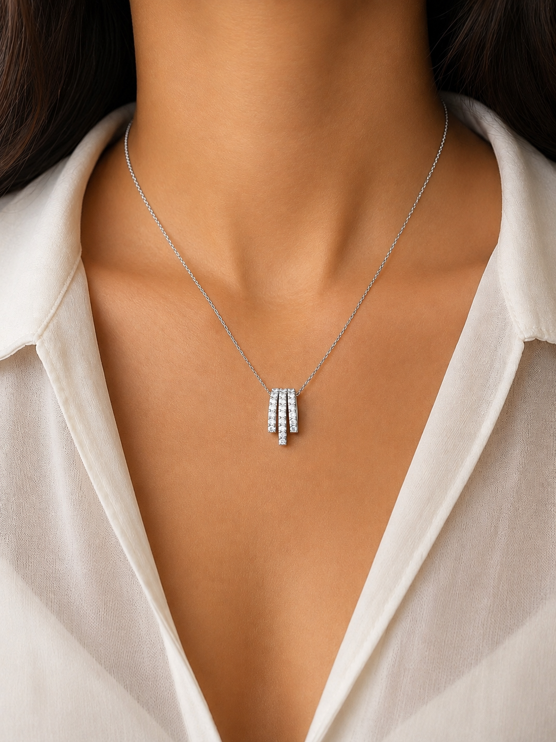 A close-up of a model wearing a delicate silver necklace with a triple-bar pendant set with small clear stones, paired with a white collared blouse.